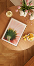 una mesa de madera con una imagen enmarcada de una flor, un frutero y un jarrón con flores rosas.
