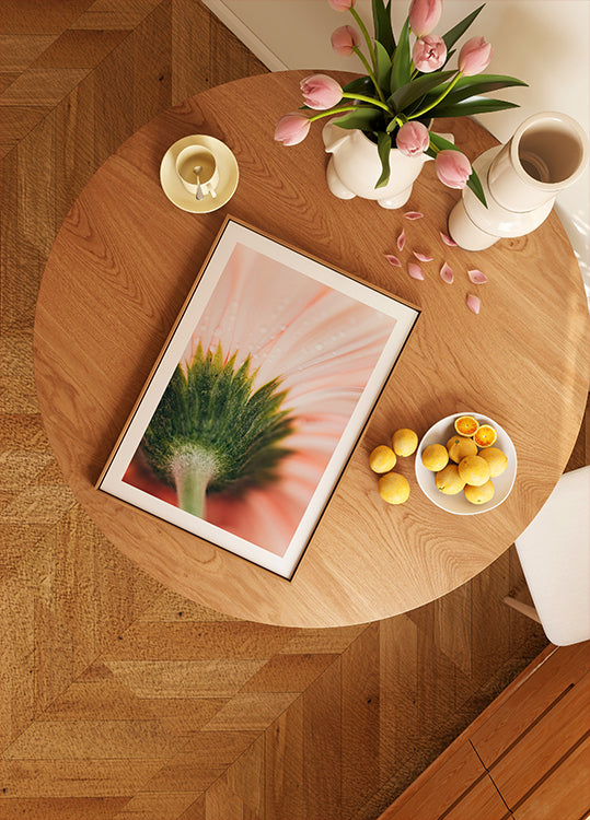 una mesa de madera con una imagen enmarcada de una flor, un frutero y un jarrón con flores rosas.