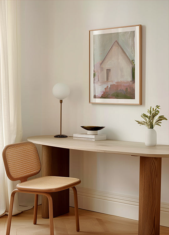 un espacio de trabajo moderno y minimalista con un escritorio de madera, una silla tejida, una lámpara y un cuadro enmarcado de una casa.