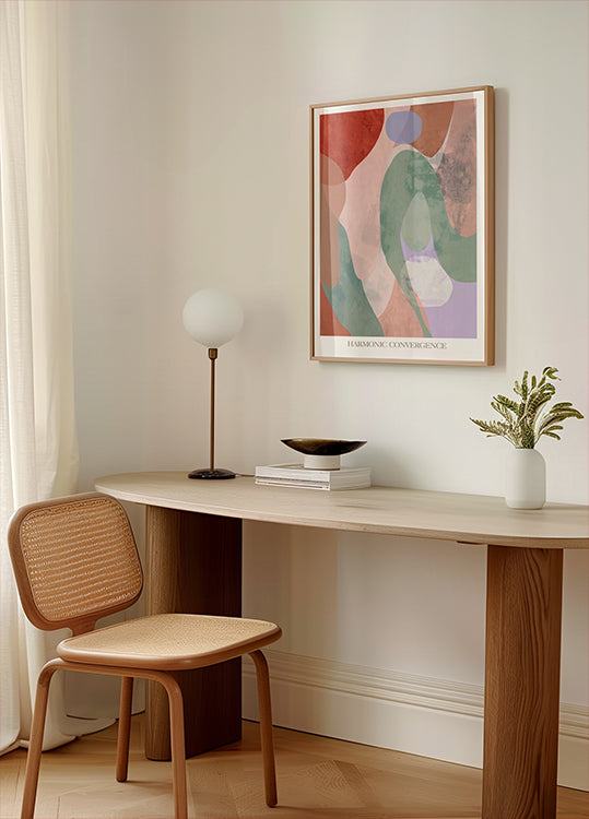 un espacio de trabajo minimalista con un escritorio de madera, una silla tejida, una lámpara y un cuadro abstracto enmarcado en la pared.
