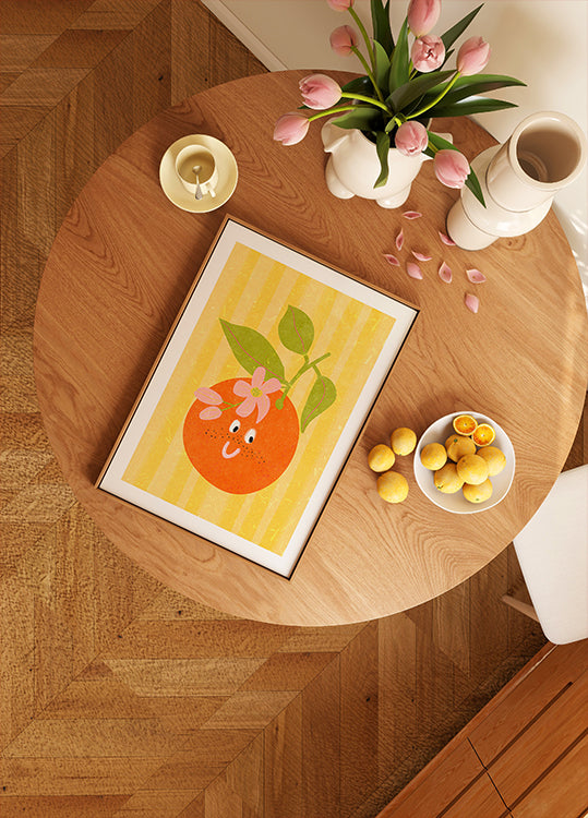 una mesa de madera con una imagen enmarcada de una naranja, un cuenco de limones, un jarrón con tulipanes rosas y una vela.