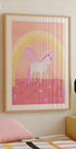 un póster enmarcado de un unicornio con una combinación de colores rosa y blanco, sobre un fondo rosa y amarillo con un arco de arcoíris.