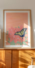 una pintura enmarcada de una mariposa sobre una flor rosa, expuesta en un gabinete o estante de madera.