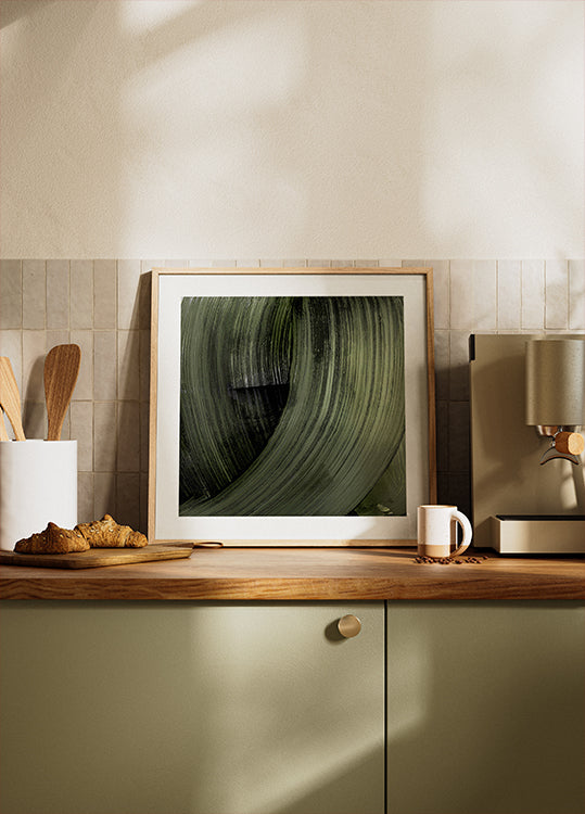 una fotografía enmarcada de una hoja verde sobre la encimera de la cocina, con una cafetera y otros artículos de cocina visibles al fondo.