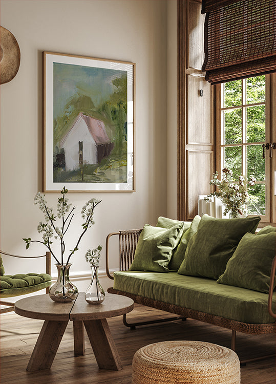 una acogedora sala de estar con un gran ventanal, un sofá verde, una mesa de centro de madera y un cuadro enmarcado de una casa.