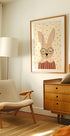 una acogedora sala de estar con un sillón beige, una cómoda de madera y una imagen enmarcada de un conejo con gafas.