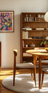 una sala de estar acogedora y bien organizada con una estantería de madera, una mesa redonda de madera y una silla de madera. La habitación tiene un ambiente cálido y acogedor, con un cuadro en la pared y un frutero sobre la mesa.